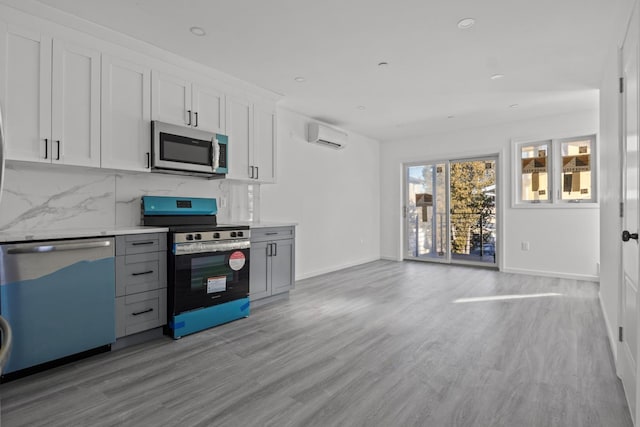 kitchen featuring appliances with stainless steel finishes, white cabinetry, a wall unit AC, tasteful backsplash, and light wood-type flooring