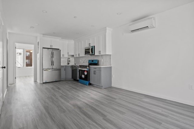 kitchen featuring white cabinetry, a wall mounted air conditioner, appliances with stainless steel finishes, light hardwood / wood-style floors, and decorative backsplash