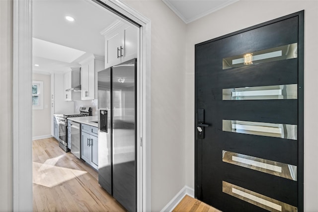 interior space with ornamental molding, stainless steel appliances, light hardwood / wood-style floors, and white cabinets