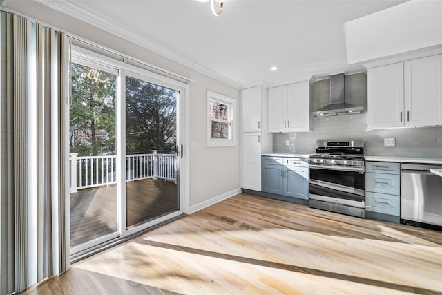 kitchen featuring wall chimney exhaust hood, crown molding, appliances with stainless steel finishes, white cabinets, and backsplash