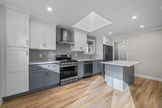 kitchen featuring gray cabinets, a skylight, a center island, stainless steel appliances, and wall chimney exhaust hood