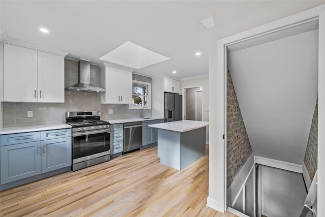 kitchen with wall chimney range hood, sink, stainless steel appliances, white cabinets, and light wood-type flooring