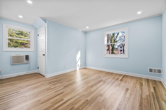 empty room with ornamental molding, a healthy amount of sunlight, a wall mounted AC, and light hardwood / wood-style flooring