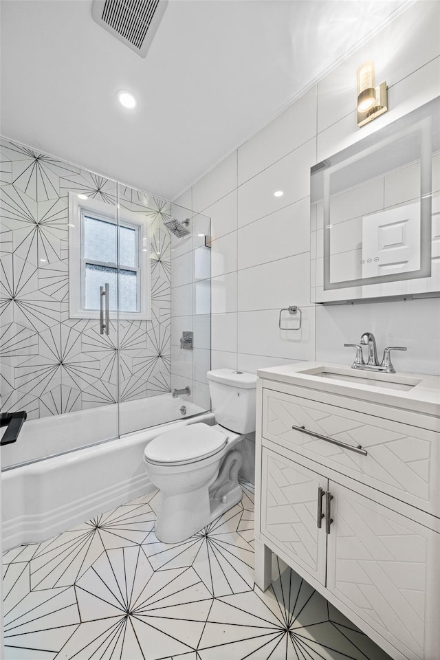 full bathroom featuring tile patterned floors, toilet, tiled shower / bath, tile walls, and vanity