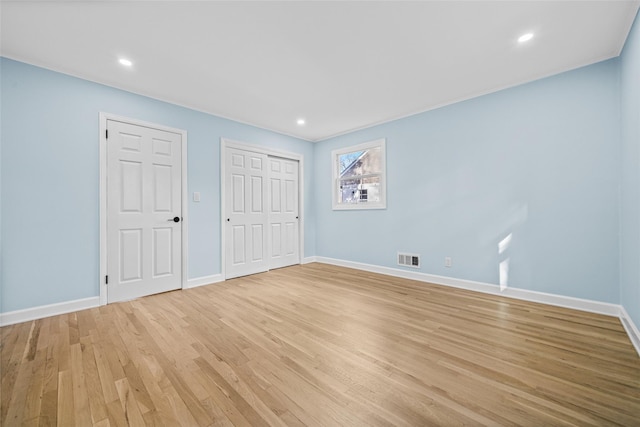 unfurnished bedroom featuring multiple closets and light wood-type flooring