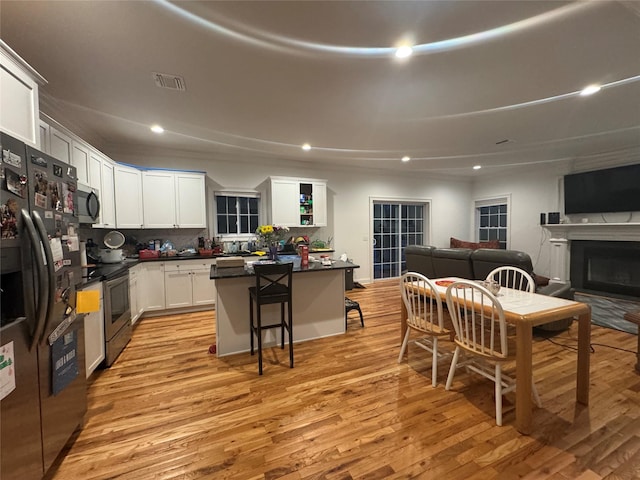 kitchen with a kitchen bar, white cabinetry, a center island, stainless steel appliances, and light hardwood / wood-style floors