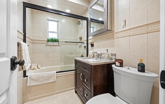 full bathroom featuring tile patterned flooring, toilet, shower / bath combination with glass door, tile walls, and vanity