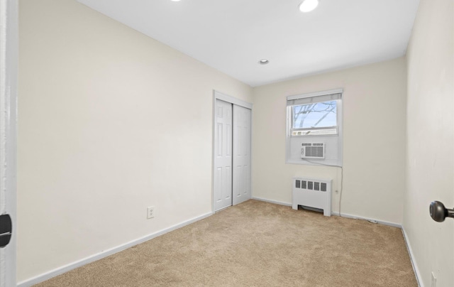 unfurnished bedroom featuring cooling unit, light carpet, a closet, and radiator heating unit