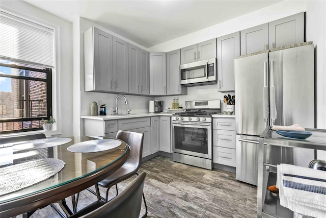 kitchen with sink, gray cabinetry, dark hardwood / wood-style flooring, decorative backsplash, and stainless steel appliances