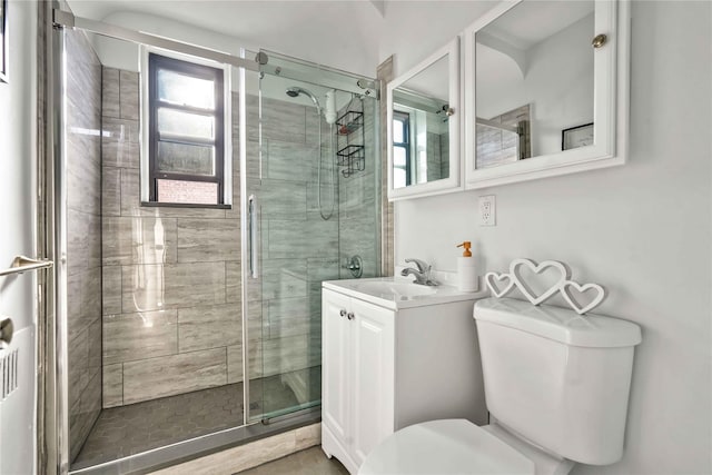 bathroom featuring a shower with door, vanity, and toilet