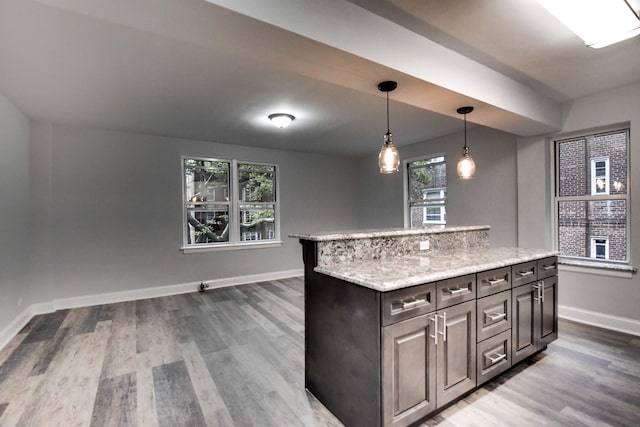 kitchen with dark brown cabinetry, a center island, hanging light fixtures, hardwood / wood-style flooring, and light stone countertops