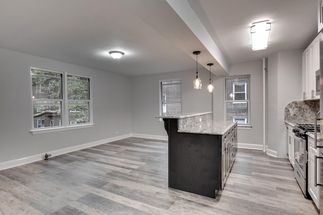 kitchen featuring decorative light fixtures, white cabinetry, a center island, light stone counters, and stainless steel gas range