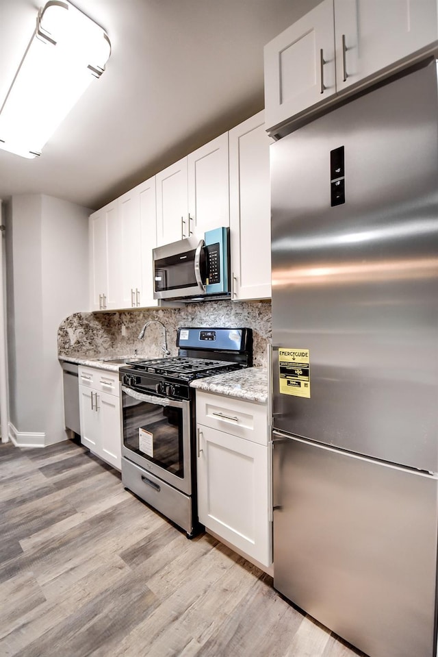 kitchen featuring stainless steel appliances, white cabinetry, light stone counters, and light hardwood / wood-style flooring