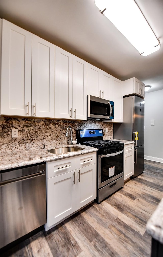 kitchen with sink, appliances with stainless steel finishes, white cabinetry, light hardwood / wood-style floors, and light stone countertops