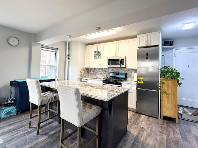 kitchen featuring hanging light fixtures, stainless steel appliances, light stone counters, tasteful backsplash, and white cabinets