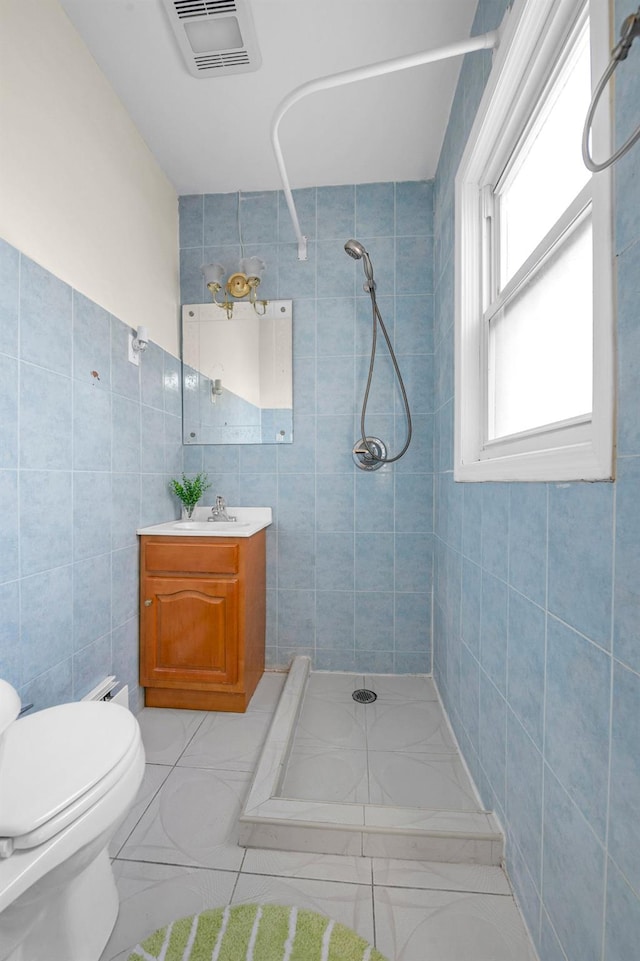 bathroom featuring tile patterned floors, toilet, tile walls, a tile shower, and vanity