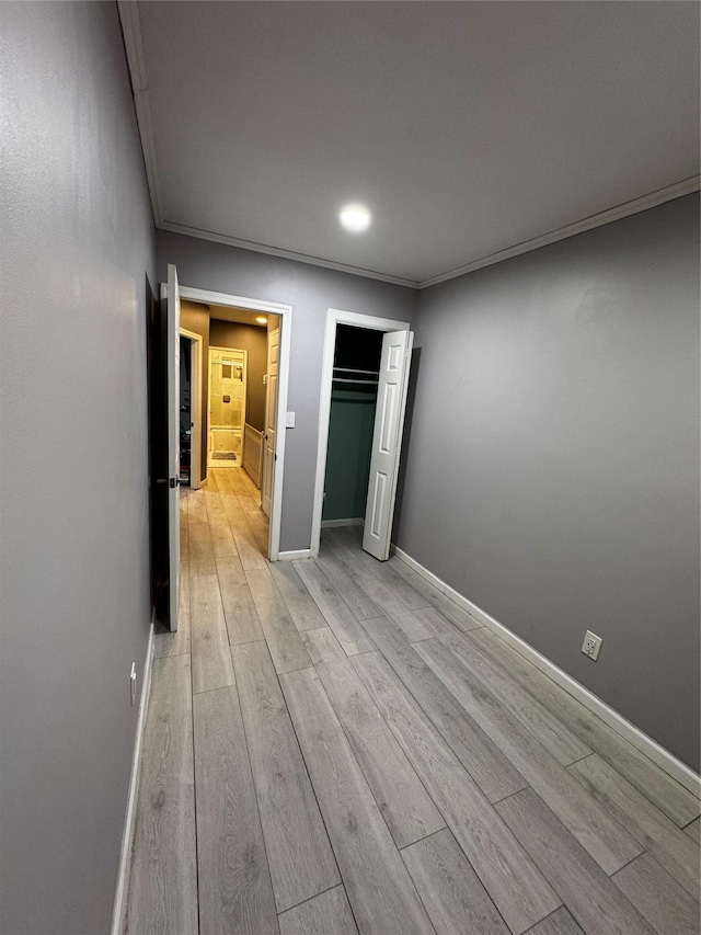 unfurnished bedroom featuring crown molding, light hardwood / wood-style floors, and a closet