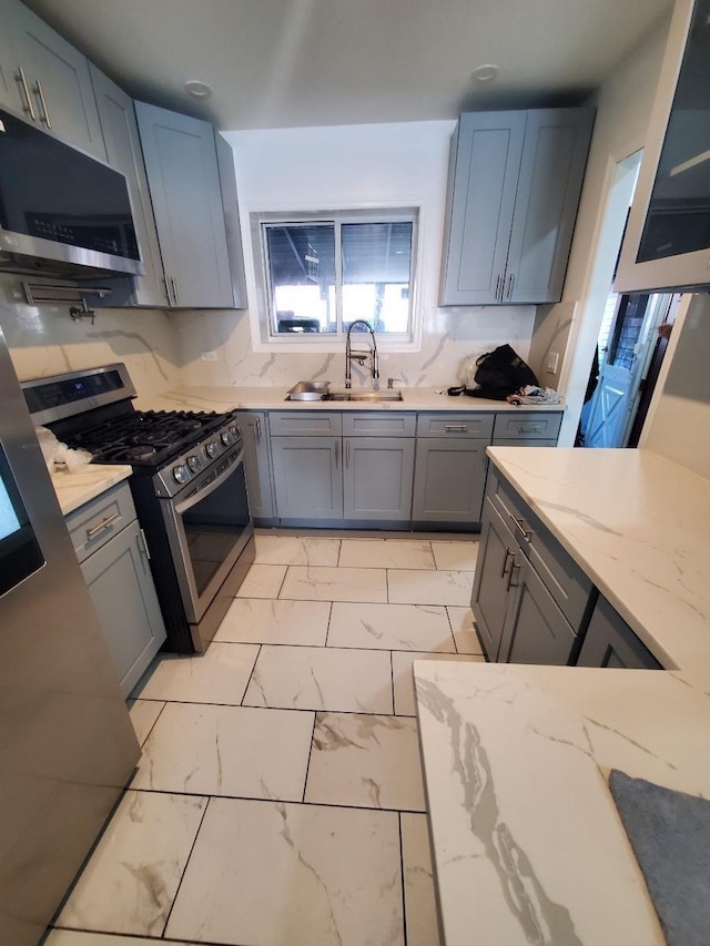 kitchen with sink, gray cabinets, stainless steel appliances, and light stone countertops