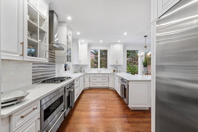 kitchen with dark wood-type flooring, white cabinetry, built in appliances, pendant lighting, and light stone countertops