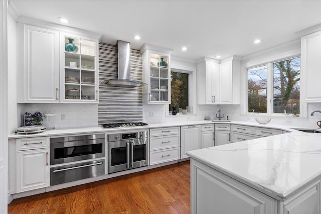 kitchen with appliances with stainless steel finishes, wall chimney exhaust hood, decorative backsplash, and white cabinets