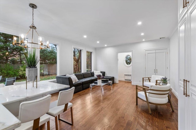 living room featuring radiator, crown molding, light hardwood / wood-style floors, and a chandelier