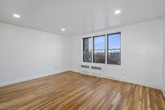 spare room featuring radiator heating unit, baseboards, wood-type flooring, and recessed lighting