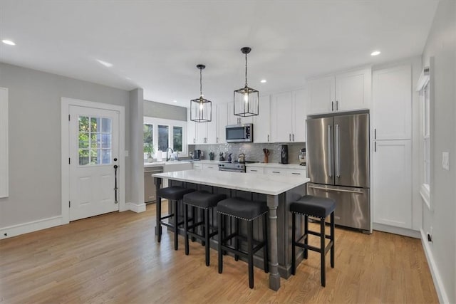 kitchen featuring pendant lighting, appliances with stainless steel finishes, a center island, light hardwood / wood-style floors, and white cabinets