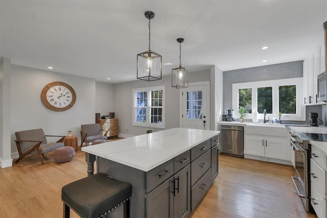 kitchen with appliances with stainless steel finishes, white cabinetry, hanging light fixtures, a center island, and light hardwood / wood-style flooring