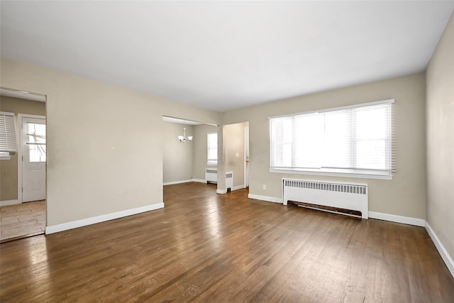 unfurnished living room featuring dark wood-type flooring, radiator heating unit, and a chandelier