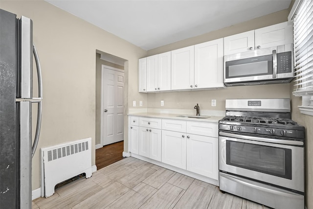 kitchen with white cabinetry, stainless steel appliances, radiator, and sink