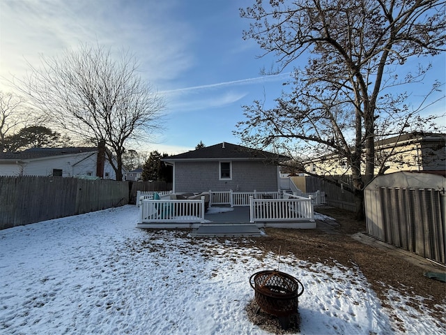 snow covered back of property with a deck and a fire pit