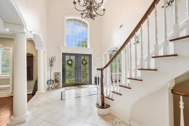 entrance foyer featuring decorative columns, a high ceiling, light tile patterned floors, an inviting chandelier, and french doors