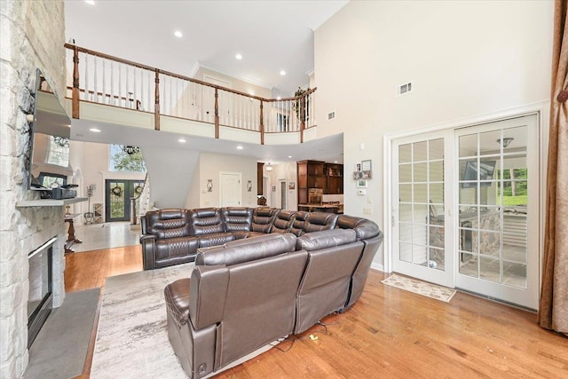 living room featuring a high ceiling, a stone fireplace, light wood-type flooring, and french doors