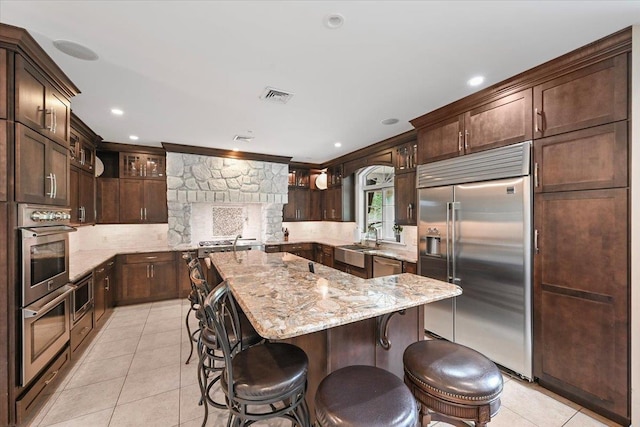 kitchen with dark brown cabinetry, sink, light stone counters, a kitchen island, and stainless steel appliances