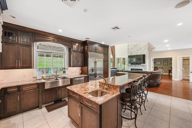 kitchen with light stone counters, sink, a center island with sink, and appliances with stainless steel finishes