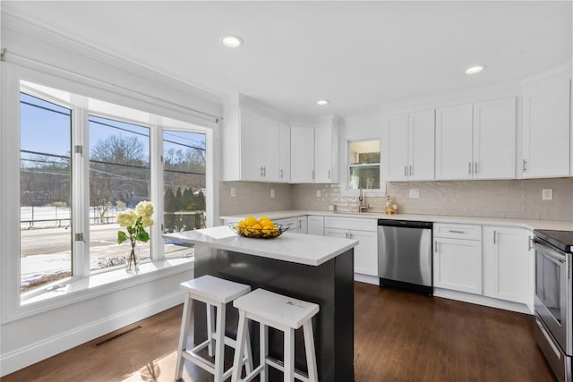 kitchen featuring appliances with stainless steel finishes, tasteful backsplash, white cabinetry, dark hardwood / wood-style flooring, and a center island