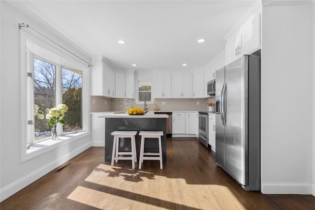 kitchen with appliances with stainless steel finishes, white cabinetry, a kitchen breakfast bar, a center island, and a wealth of natural light