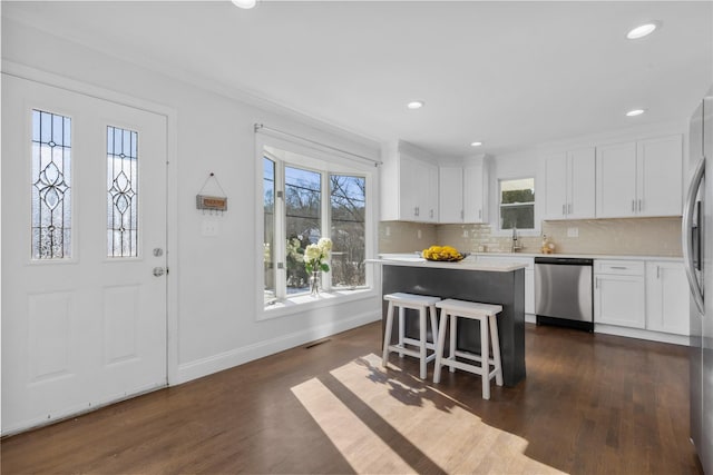 kitchen with dark wood-type flooring, a breakfast bar area, a center island, appliances with stainless steel finishes, and white cabinets