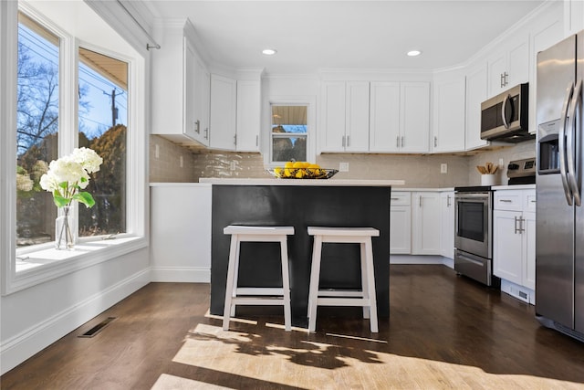 kitchen featuring white cabinetry, appliances with stainless steel finishes, dark hardwood / wood-style floors, a kitchen breakfast bar, and backsplash