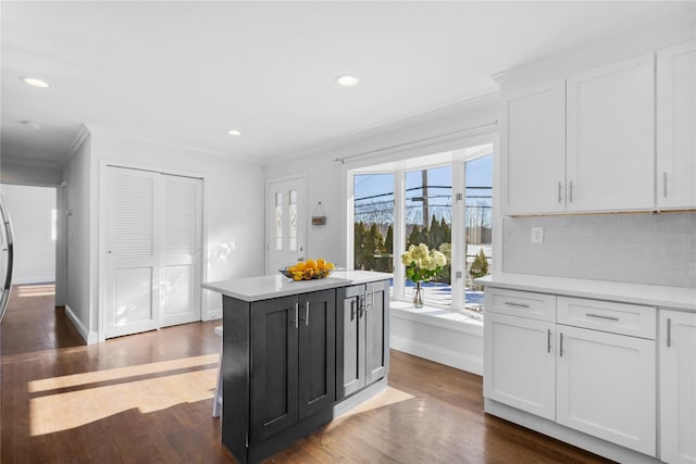 kitchen with crown molding, dark wood-type flooring, white cabinetry, backsplash, and a center island