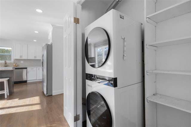 clothes washing area with dark hardwood / wood-style floors, stacked washing maching and dryer, and sink