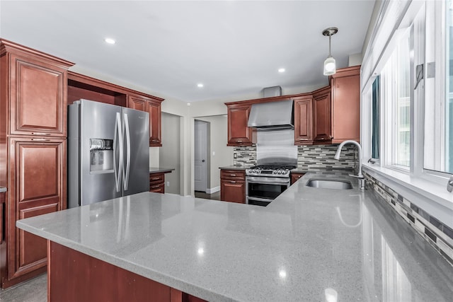 kitchen with wall chimney exhaust hood, sink, decorative light fixtures, appliances with stainless steel finishes, and backsplash