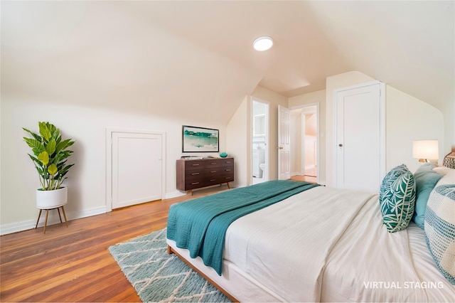 bedroom with ensuite bathroom, lofted ceiling, and hardwood / wood-style floors