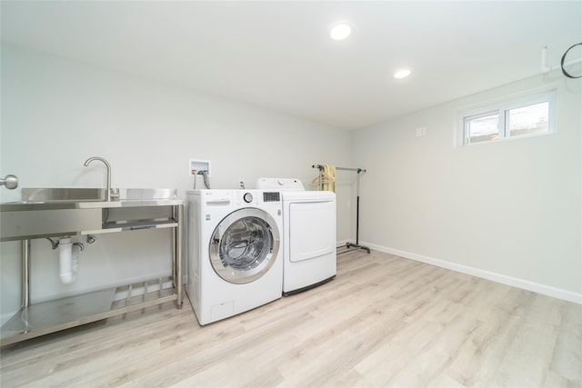 laundry area featuring sink, washing machine and clothes dryer, and light hardwood / wood-style flooring