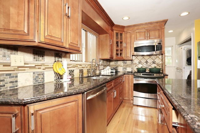 kitchen featuring sink, stacked washer and dryer, stainless steel appliances, dark stone counters, and light wood-type flooring