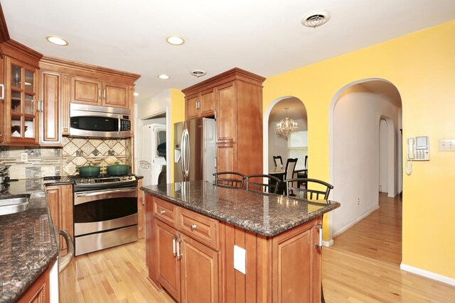 kitchen featuring dark stone countertops, backsplash, a center island, light hardwood / wood-style floors, and stainless steel appliances