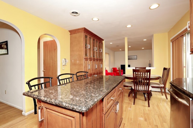 kitchen with stainless steel dishwasher, dark stone counters, a kitchen island, and light hardwood / wood-style flooring