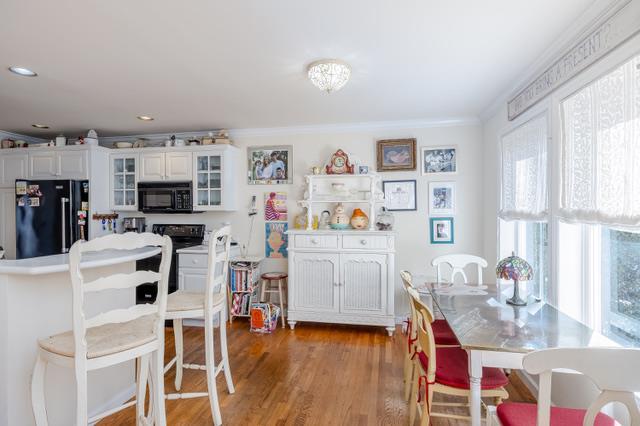 kitchen with white cabinetry, crown molding, black appliances, and hardwood / wood-style floors