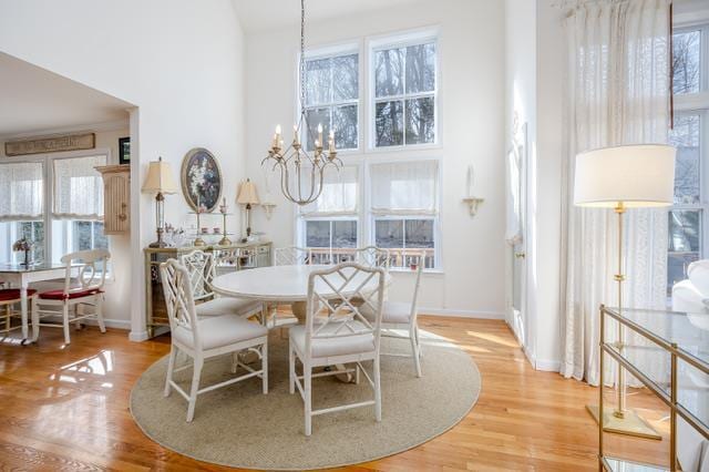 dining space featuring light wood-type flooring, a chandelier, a towering ceiling, and a healthy amount of sunlight