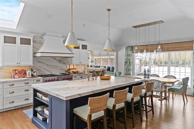 kitchen featuring white cabinetry, an island with sink, custom range hood, and backsplash